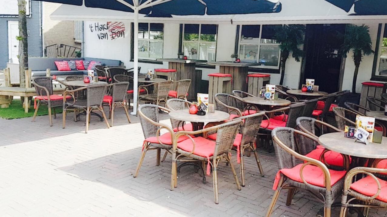 Het terras van ’t Hart van Son met parasols, rieten stoelen en het logo op de witte muur