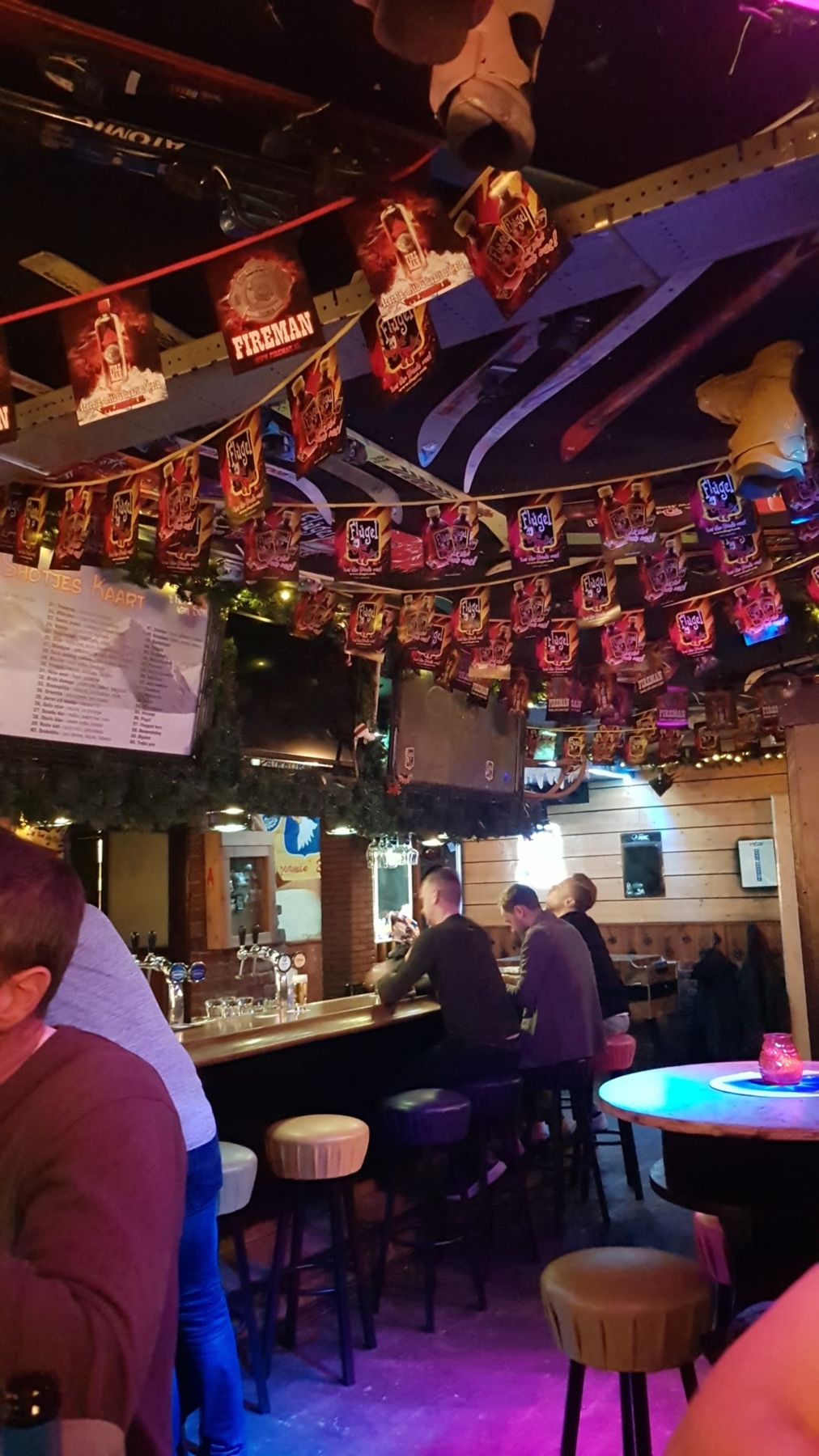 Avond in ’t Hart van Son: ski’s en vlaggetjes aan het plafond, gasten aan de bar